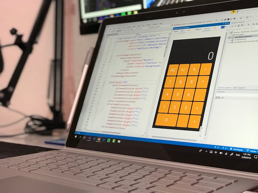 A close-up of a laptop on a desk displaying a code editor with HTML and CSS code open on the screen, alongside a large, orange calculator application. The coding interface shows text in syntax highlig